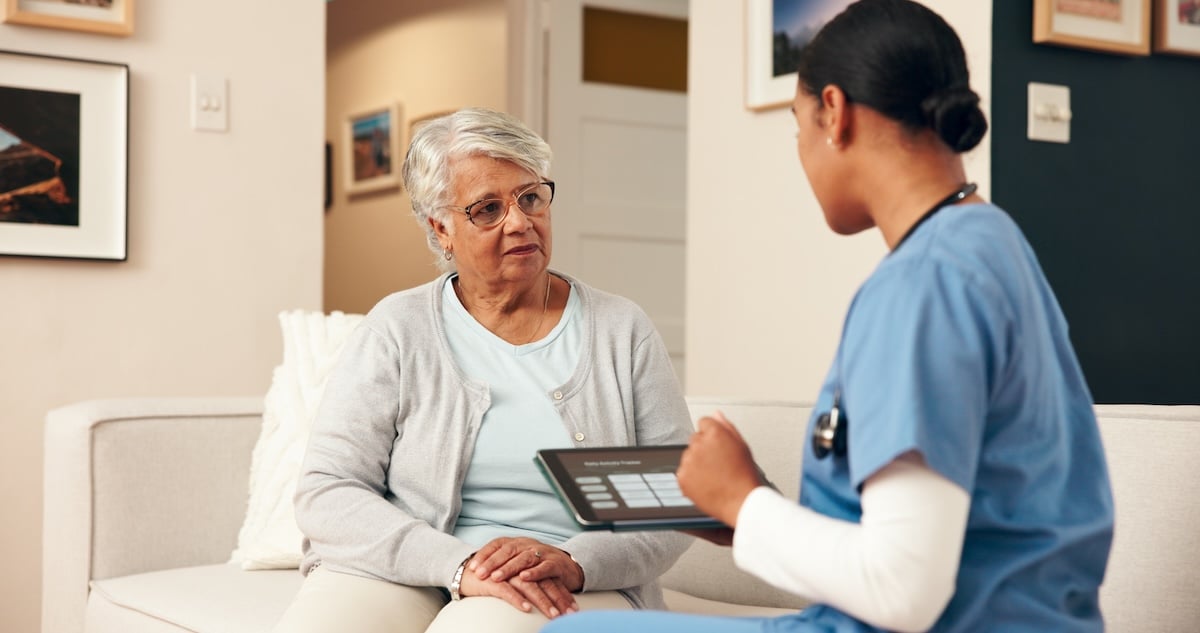 A home health aide meets with an older woman in her living room, illustrating the benefits of continuing care at home.