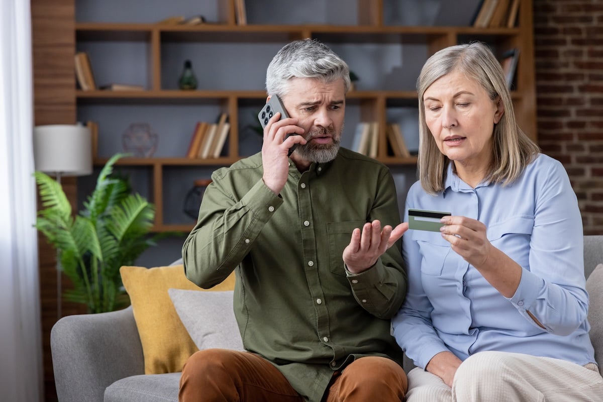 An older couple looks over a credit card while on the phone with their bank after becoming the target of a financial scam.