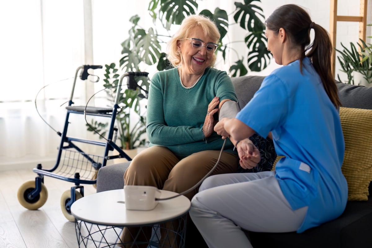 A geriatric care manager takes an older woman's blood pressure in her home.