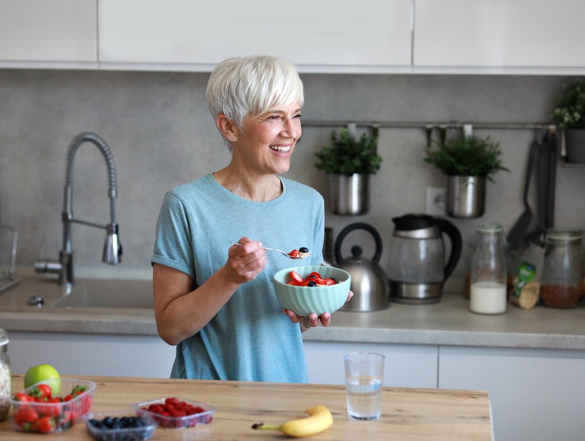 A woman eats a bowl of fruit with yogurt, illustrating one of the many gut health hacks that can help older adults feel better and live longer.