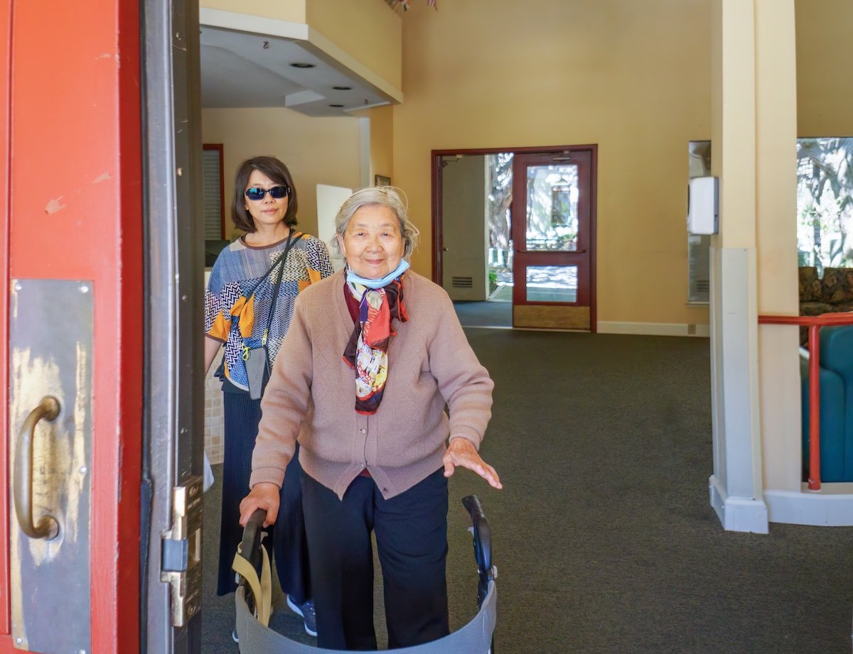 An older woman uses a walker to leave the hospital, accompanied by her daughter, illustrating the importance of hospital discharge planning.